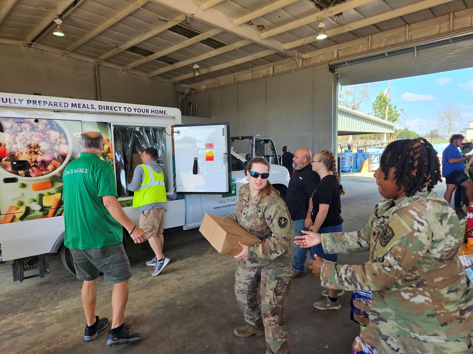 Mom’s Meals driver and U.S. service members unloading meal boxes from a Mom’s Meals truck inside a warehouse to aid Hurricane Helene relief efforts in Georgia.